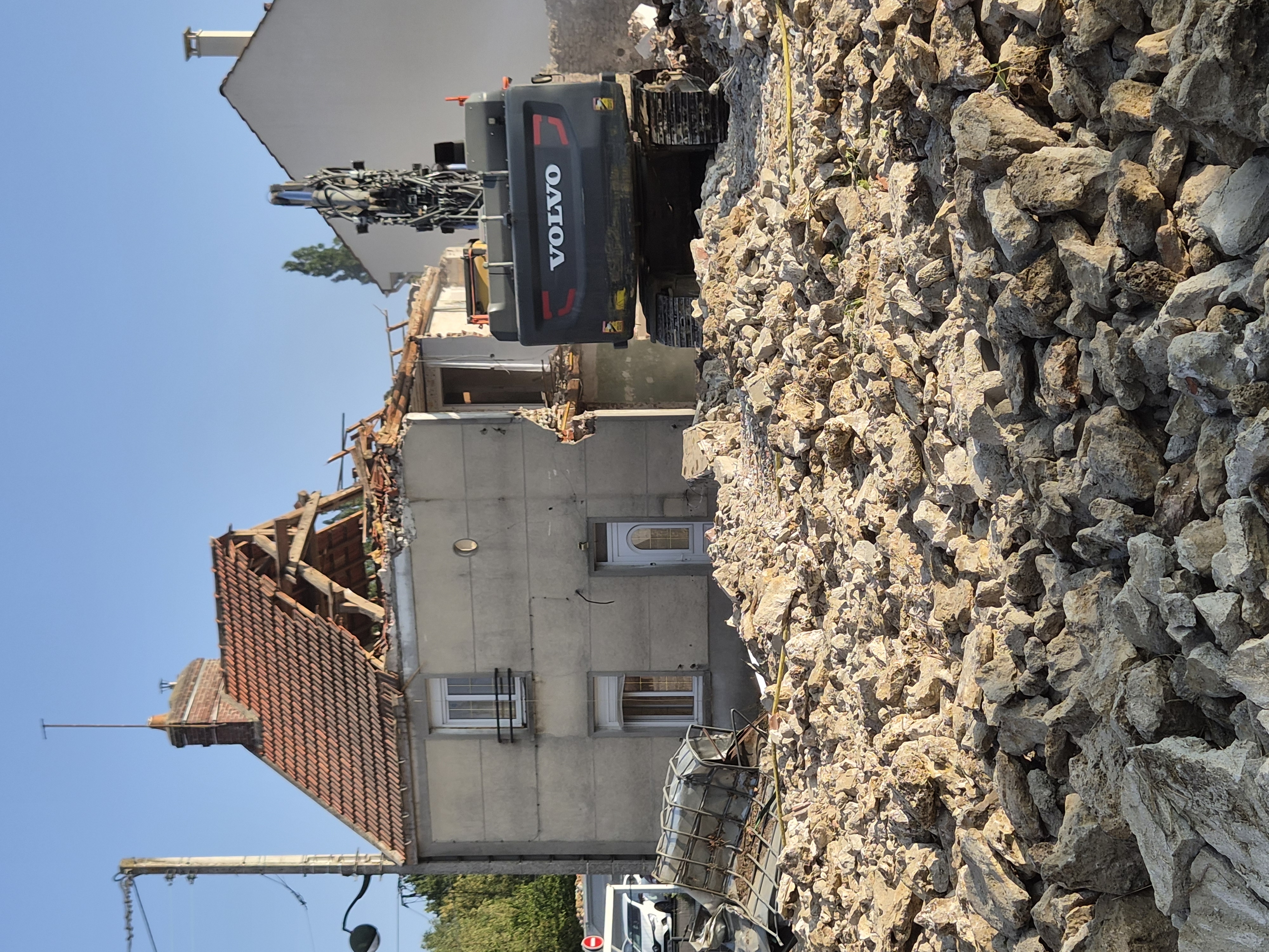 Engin de déconstruction et gravats devant une maison en cours de démolition